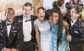 grupo de adolescentes en el baile de graduación sonriendo a la cámara con confeti cayendo a su alrededor