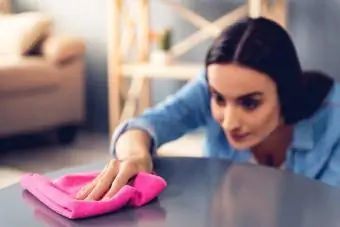 Moteris, valydama baldus namuose, naudoja medžiaginę dulkių šluostę