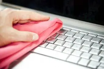 Frau reinigt Laptop mit Staubwedel