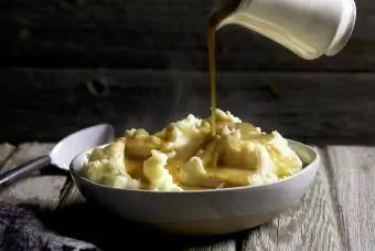 Kruik jus wordt op een kom met stomende aardappelpuree gegoten