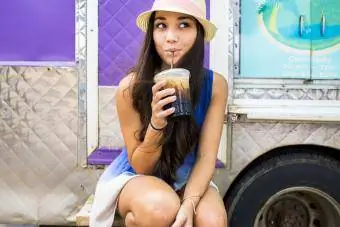 Mujer bebiendo café helado cerca del carrito de comida