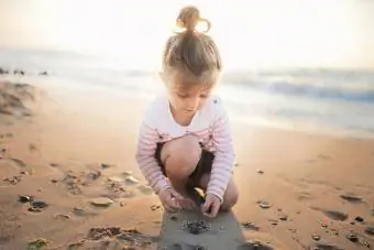პატარა გოგონა მზის ჩასვლისას სანაპიროზე ქვებს აგროვებს