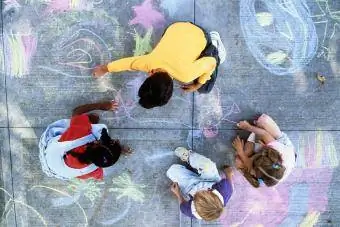 Четири деца рисуват с тебешир върху тротоара
