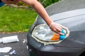 Home netejant els fars del cotxe enganxats per protegir el fregament de pintura amb una tovallola blava