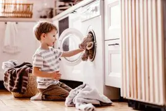 Berniukas skalbykloje su skalbimo mašina ir meškiuku