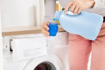 Mâinile de sex feminin turnând detergent în capacul sticlei