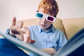 Zvedavý malý chlapec nosí trojrozmerné okuliare a číta knihu