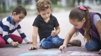 Niños y niñas hispanos dibujando con tiza en la acera