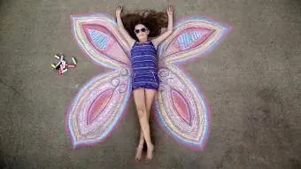 La niña se hace pasar por el centro de una mariposa dibujada en la acera con tiza.