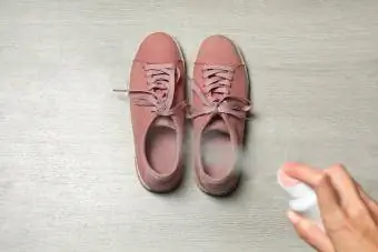 Kvinne sprøyter desinfeksjonsmiddel over et par sko