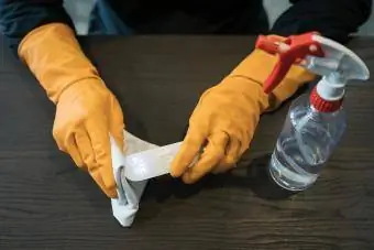 Manos con guantes protectores desinfectando pistola termómetro