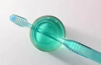Escova de dentes prestes a ser desinfetada em copo de enxaguatório bucal
