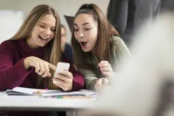 Tienermeisjes in de klas kijken naar mobiele telefoon en lachen om iemand