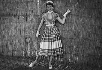 1950-yillarda qo'lqop va shlyapali yozgi chiziqli ko'ylak kiygan moda ayol