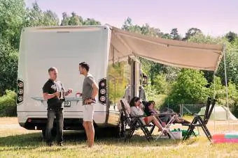 Người đàn ông lớn tuổi nói chuyện với con trai trong khi gia đình thư giãn bên ngoài xe tải ở khu cắm trại