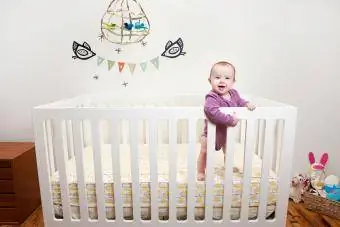 Baby im Kinderbett, umgeben von Spielzeug