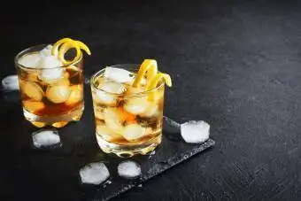 Siyah taş arka planda limon kıvrımlı buzlu viski