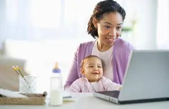 ქალი ხელში უჭირავს ბავშვს და იყენებს ლეპტოპს