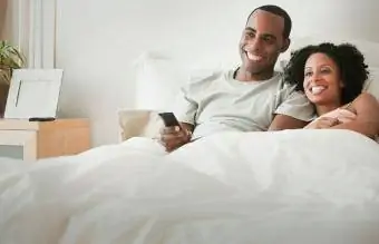 Cuplu întins în pat uitându-se la televizor