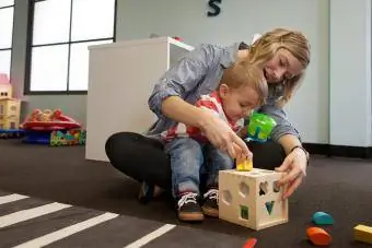 Opiekunka do dziecka i chłopiec bawiący się geometrycznym pudełkiem z puzzlami