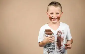 Pojken håller choklad och har smutsiga kläder