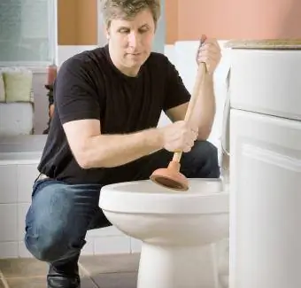 Ein Mann benutzt einen Kolben, um den Stecker einer Toilette zu Hause zu entfernen