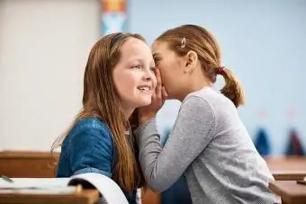 laerskoolmeisie fluister in haar vriende se oor in die klas