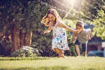 Fëmijë të lumtur që luajnë me spërkatës kopshti