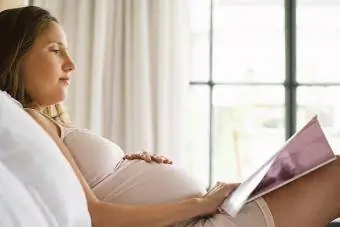 ორსული ქალი კითხულობს ჟურნალს საწოლში
