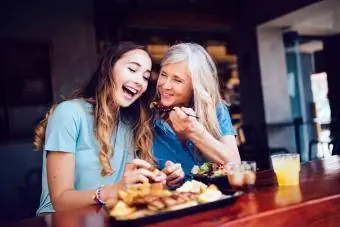 Lachende moeder en tienerdochter lunchen in een modern restaurant in de stad