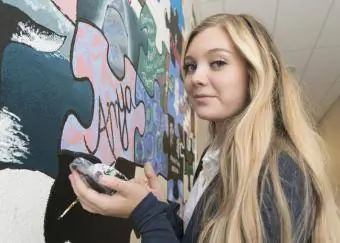 किशोर लड़की दीवार पर पेंटिंग कर रही है
