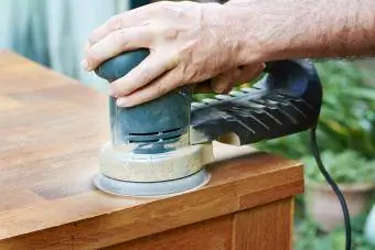 Seorang pria mengampelas meja kayu ek dengan orbital sander acak