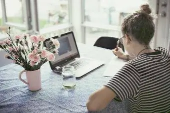 Jauna mergina prie stalo naudoja nešiojamąjį kompiuterį
