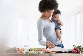 Bebek oğlunu tutarken yemek kitabı okuyan anne