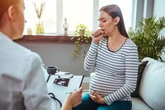 Mulher grávida jovem em visita ao médico, tossindo