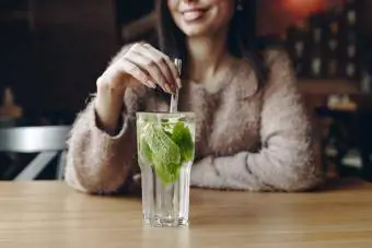 Donna che tiene la paglia in un cocktail con foglie di menta