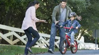 tėvai padeda sūnui važiuoti dviračiu
