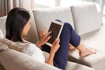 Moteris ant sofos naudojanti skaitmeninį planšetinį kompiuterį