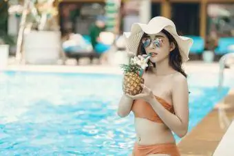 Ženska pije ananasovo pijačo ob bazenu