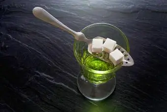 Apsint u čaši i kašikom sa kockicama šećera