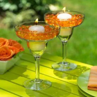 Ly cocktail chứa đầy hạt thủy tinh và một ngọn nến ở giữa