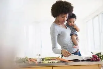 Bebek oğlunu tutarken yemek kitabı okuyan anne