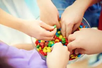 Hände von Kindern, die bunte Schokoladenbonbons aus einer Schüssel nehmen