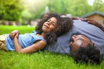 अफ़्रीकी-अमेरिकी बेटा और पिता घास पर आराम कर रहे हैं