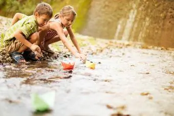 Chlapec a dievča hrajú papierové člny na rieke