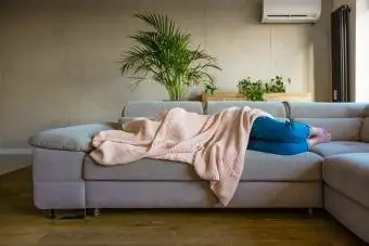 Junge Frau liegt auf dem Sofa im Wohnzimmer und ist mit einer Decke bedeckt
