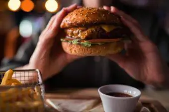 Manos sosteniendo una hamburguesa con papas fritas, salsa y bebida