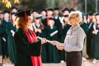 Glücklicher Senior-Professor, der einer Studentin bei ihrem Abschluss das Diplom überreicht