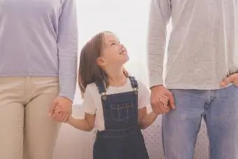 Щастливо малко момиче, което се държи за ръце с родители