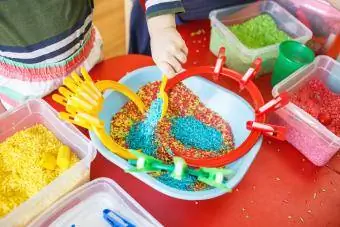 Niños pequeños jugando con contenedores sensoriales con arroz colorido en una mesa roja